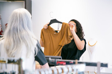 Woman buying clothes in fashion store. Cashier removing hanger from new shirt for wrapping. Back view. Shopping or purchase concept