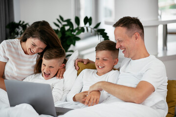 Beautiful parents with kids enjoying at home. Young family watching movie on lap top.