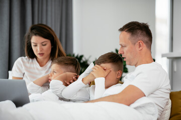 Beautiful parents with kids enjoying at home. Young family watching movie on lap top.