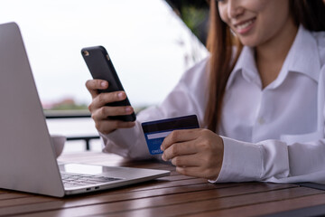 The smiling young Asian woman enjoys shopping online via a smartphone and paying online via credit card. Convenience of spending without cash. stay safe, shopping from home and Social distance