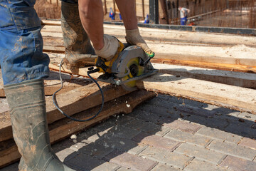 The worker is sawing the boards. The builder prepares the boards. Work at a construction site. 