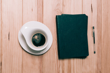Cup of coffee, notebook, and pen on a light wooden table