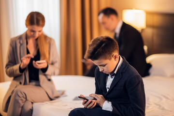 Gadget addiction concept. A family of three on a hotel bed, everyone is on their phone.