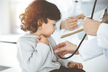 Woman-doctor examining a child patient by stethoscope in sunny clinik. Cute arab toddler at physician appointment