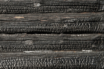 Texture (background, pattern) of a black charred log wall of a burned-out wooden house.