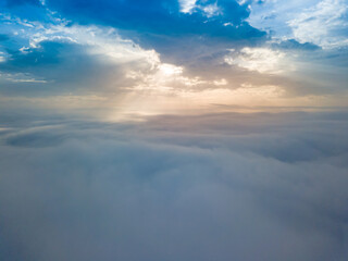 Naklejka na ściany i meble Aerial drone flight over the fog. There are thick clouds of fog below, the sun breaks through the clouds.