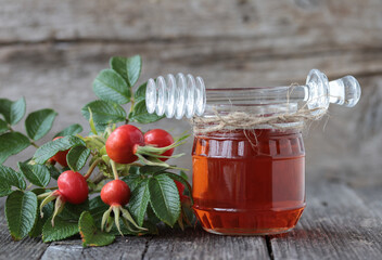 Rosehip syrup and fresh rosehip berries on a wooden background.