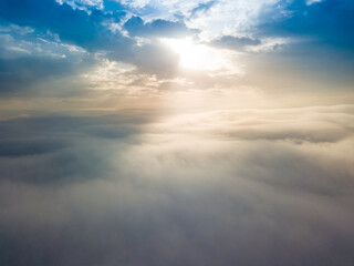 Aerial drone flight over the fog. There are thick clouds of fog below, the sun breaks through the clouds.