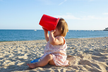 Bébé assis sur une plage joue avec un seau