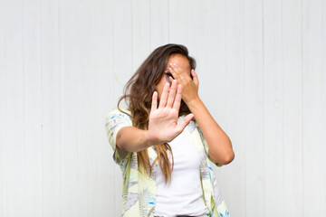 young pretty woman covering face with hand and putting other hand up front to stop camera, refusing...