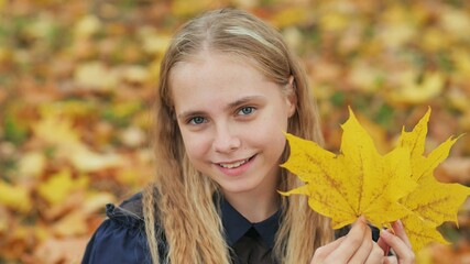 A young girl of 13 years old with autumn leaves poses in front of a photo camera.