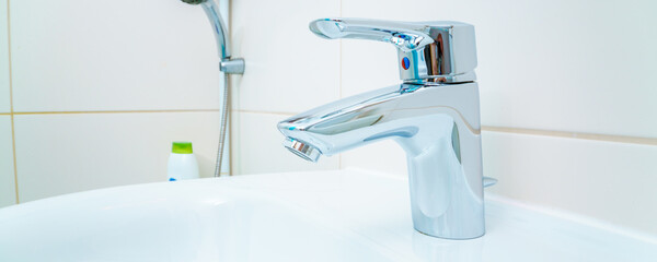 chromed metal faucet for hot and cold water,  cup with sad face for toothbrushes  in a modern...
