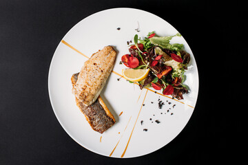 Fried fish in white plate on a black background with lime. 