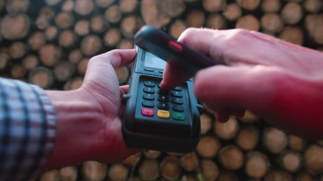 Close-up Of A Bank Terminal Paying For Lumber At A Sawmill The Buyer Applies His Phone For Online Payment. Cashless Payments At The Enterprise.