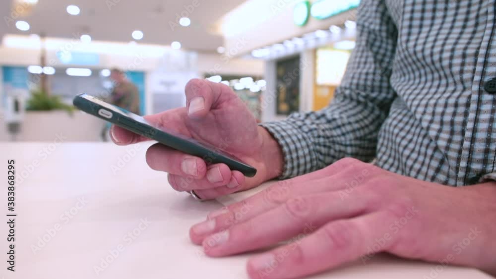 Poster close-up of a man's hands using the phone in a shopping mall. transfer of information over a distanc