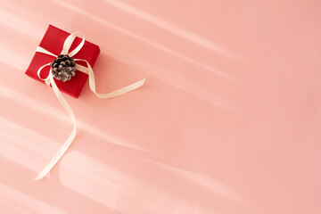 
red gift box  with ribbon on pink background with hard shadows