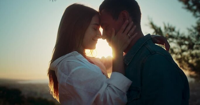 Side close up portrait shot of happy couple smiling gently touching faces at sunrise sun, two young woman and man embracing love moment of person feelings and emotions at wonderful summer date