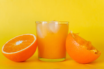 Glass of orange juice with ice and an orange cut in half. Yellow background.
