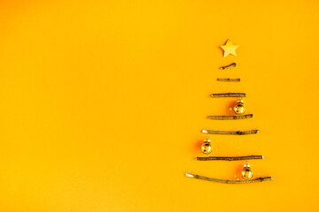 Creative Christmas tree made of wooden sticks. Minimal design on golden orange background.