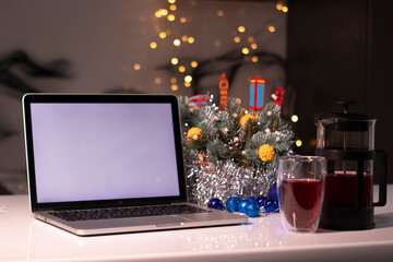 Laptop with white screen next to french press and tea near new years decorations. christmas theme template.