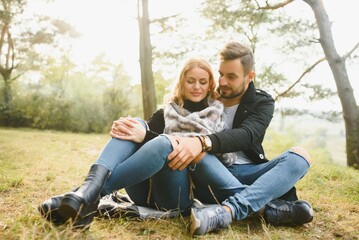 Naklejka na ściany i meble Couple in love sitting on autumn fallen leaves in a park, enjoying a beautiful autumn day.