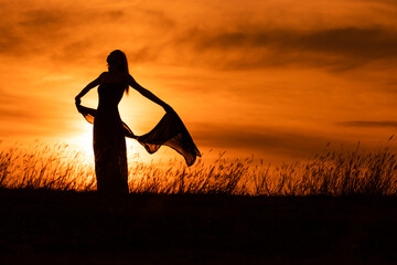 Happy woman dancing and holding scarf while enjoys spending time at sunset.