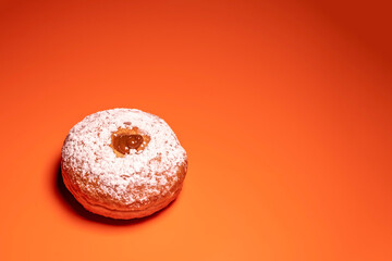 Sufganiya for Jewish holiday Hanukkah on orange background with copy space.