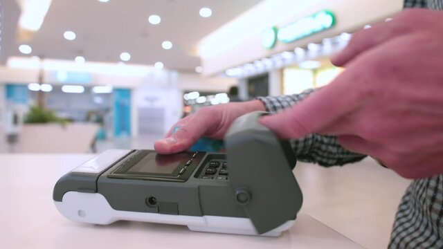 A man makes a payment by credit card at a store. Inserts a card into the terminal, enters a pin. Cashless settlement is the rule of social distance.