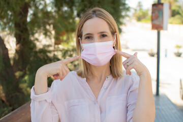 Happy young woman wearing facial mask for virus protection standing outdoors on sunny spring day.