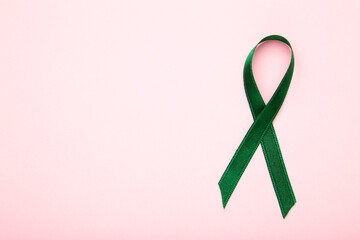 Healthcare and medicine concept. Green organ transplant awareness ribbon on pink background.