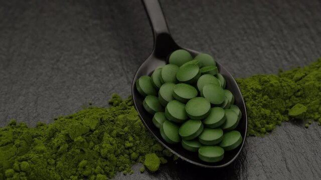 rotating chlorella or spirulina superfoods tablets in wooden spoon and powder on background. rotation to left