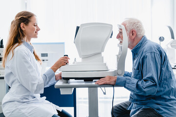 Woman oculist examining old man`s sight with ophthalmic tool - obrazy, fototapety, plakaty