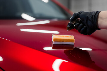 Car detailing - Man applies nano protective coating or wax on red car. Covering car bonnet with a liquid glass polish. - 383882069
