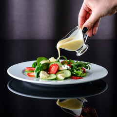 a woman's hand pours sauce on a fresh salad of cucumbers, strawberries and cheese