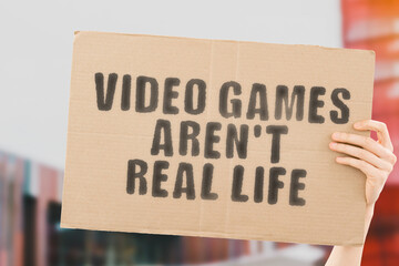 The phrase " Video games aren’t real life " on a banner in men's hand with blurred background. Addiction. Computer. Addicted. Gamer. Play. Hobby