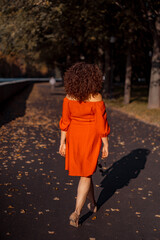 A beautiful woman with curly dark hair in a red dress walks through the autumn city. Autumn mood,...