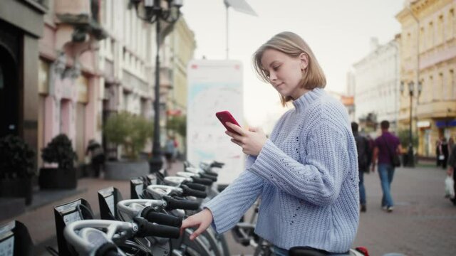 Tourist girl takes bike bicycle in sharing parking, tourist phone application. Eco transport. Friendly transportation methods.