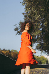 A beautiful woman with curly dark hair in a red dress walks through the autumn city. Autumn mood,...