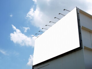 Blank billboard beside a building. With lamps on top can be advertised for displaying. On a blue sky background with white clouds. Selective focus