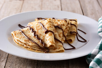 Sweet crepes with chocolate on wooden table