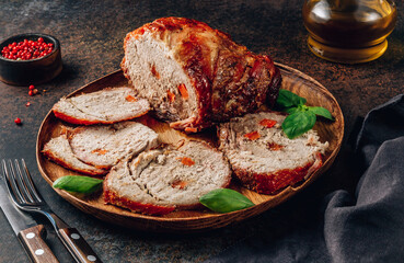 Roasted sliced pork ham on a wooden plate on a dark rustic background.