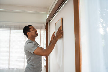 African American man decorating and putting picture frame on the wall at home