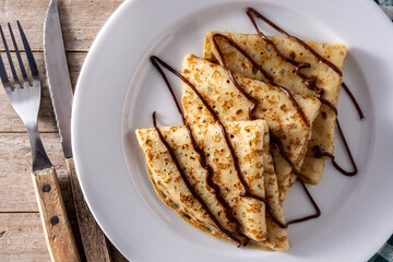 Sweet crepes with chocolate on wooden table