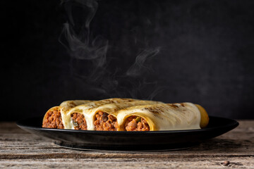 Hot meat cannelloni pasta on rustic wooden table	 and black background