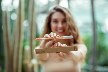 Pretty young woman in beige clothes showing a toothbrush and smiling