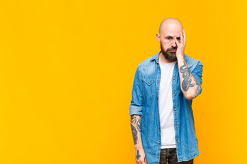 young bald and bearded man feeling bored, frustrated and sleepy after a tiresome, dull and tedious task, holding face with hand