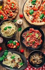 Table of italian meals on plates Pizza, pasta, ravioli, carpaccio, mushroom risotto, caprese salad and tomato bruschetta on rustic wooden background.