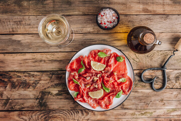 White plate with carpaccio of beef with baby arugula, lime and white wine on rustic wooden background.