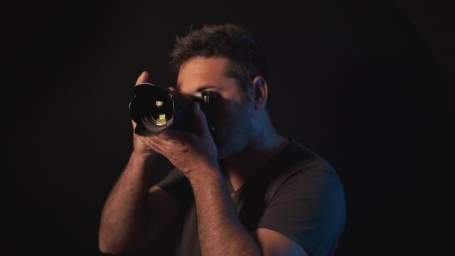 Professional photographer panning and following the subject and taking a picture. Man photography enthusiast using a mirrorless DSLR camera in a dark studio with black background.