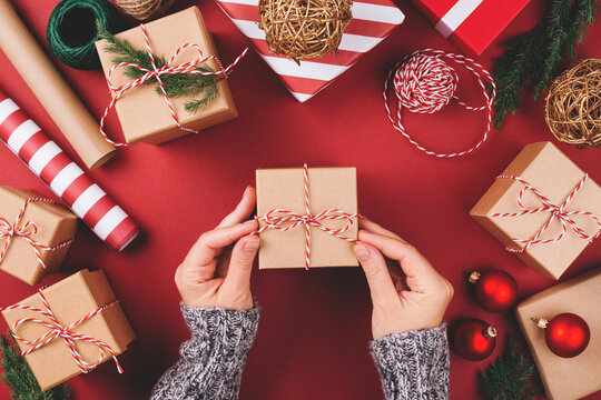 Christmas background with gift boxes and decorations on red. Preparation for holidays. Top view with copy space. Woman's hands tying gift box.